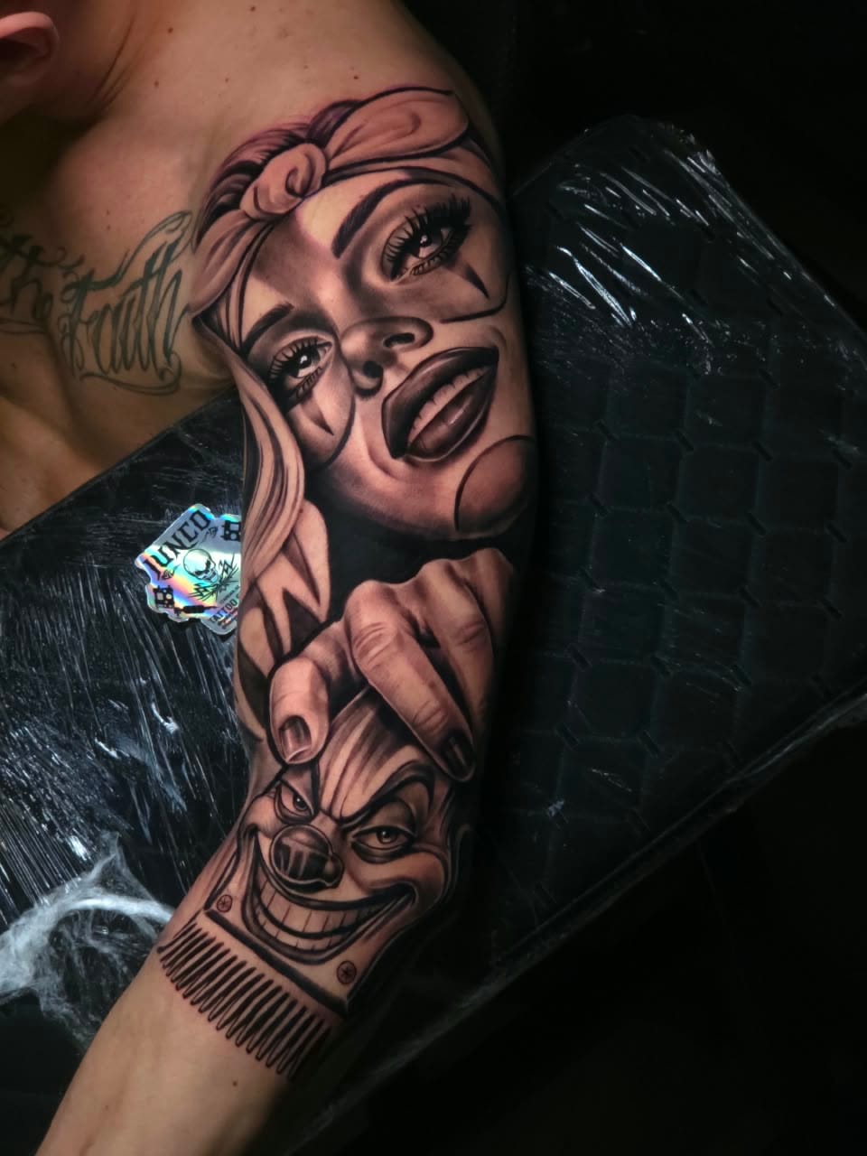 Tatuagem chicana no braço com rosto feminino de bandana, mão e palhaço, por Gabriel Junco
