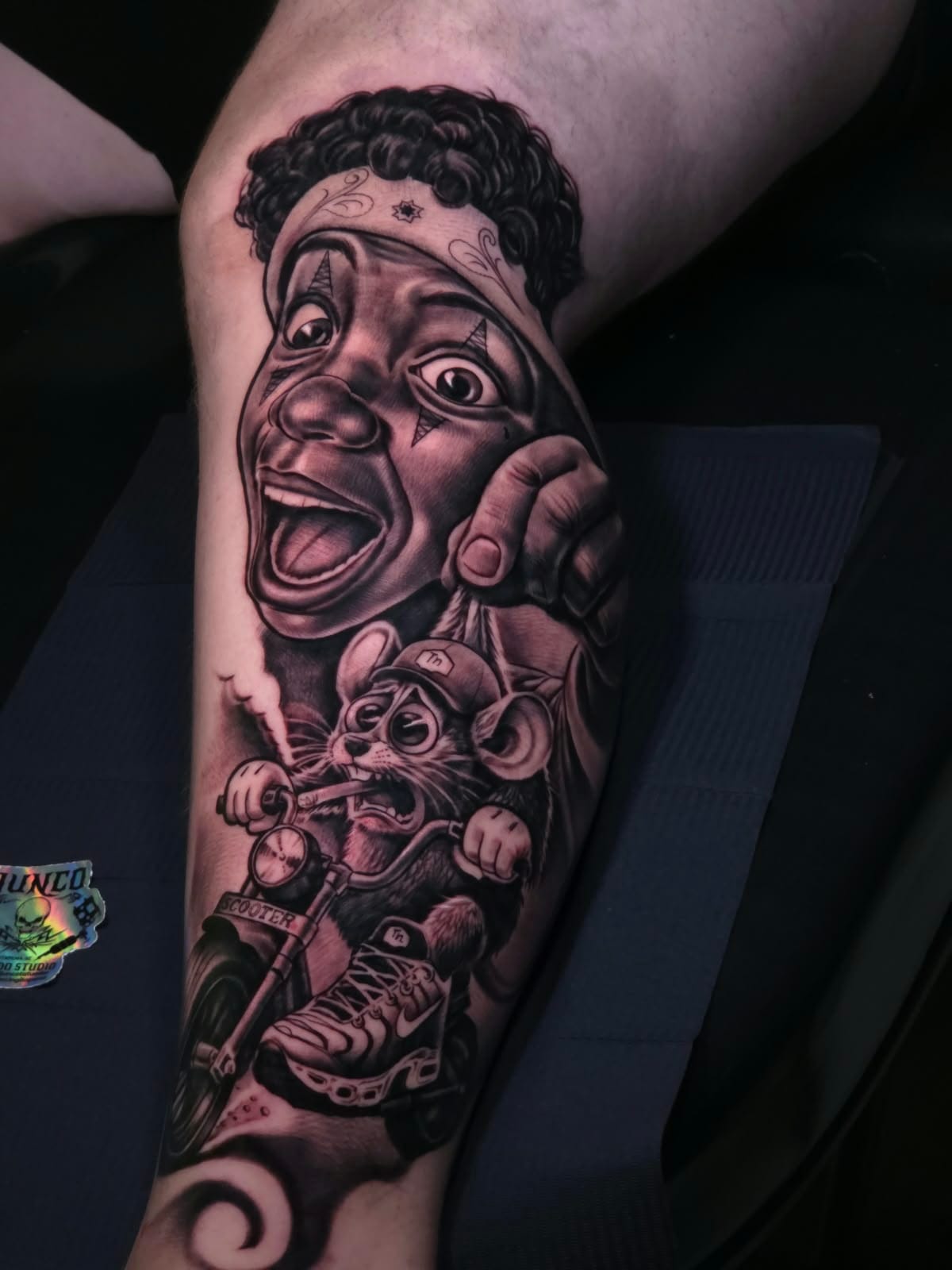 Tatuagem na perna com rosto de palhaço de bandana e rato pilotando uma scooter