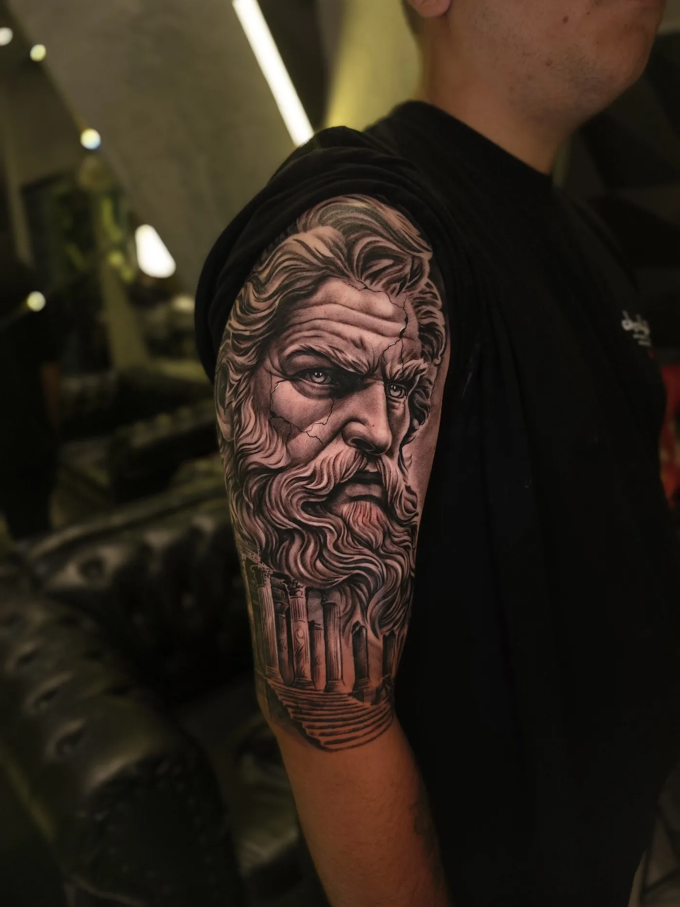 Tatuagem de estátua grega de Zeus em realismo preto e cinza no braço