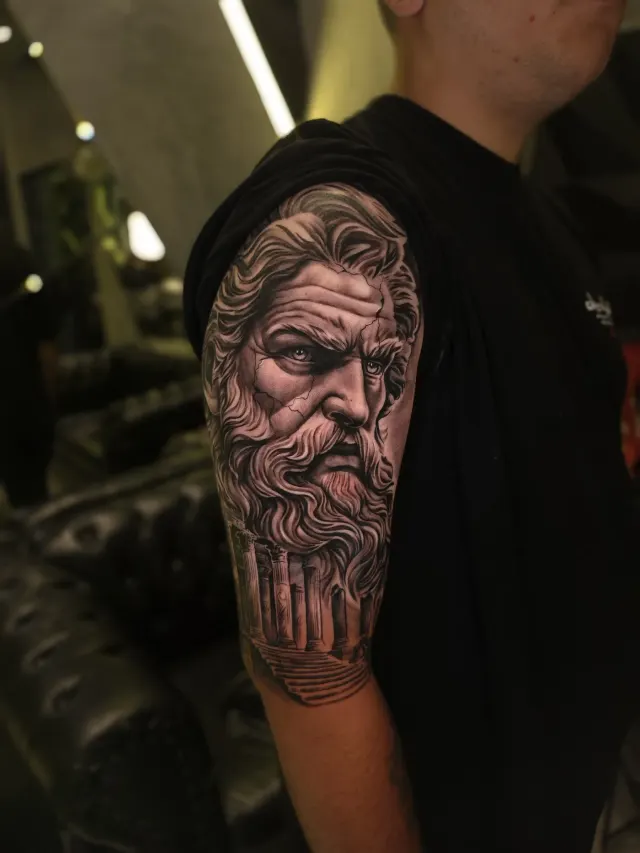 Tatuagem de estátua grega de Zeus em realismo preto e cinza no braço