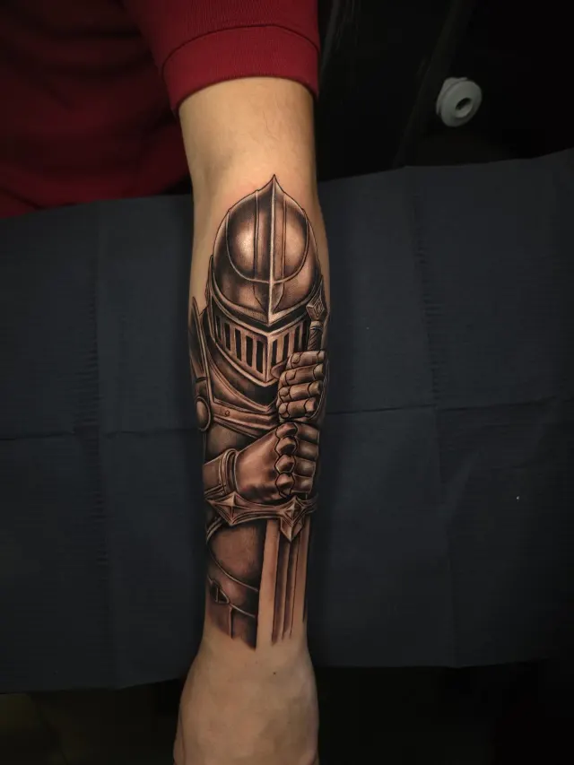 Tatuagem de armadura de cavaleiro com espada em realismo no antebraço
