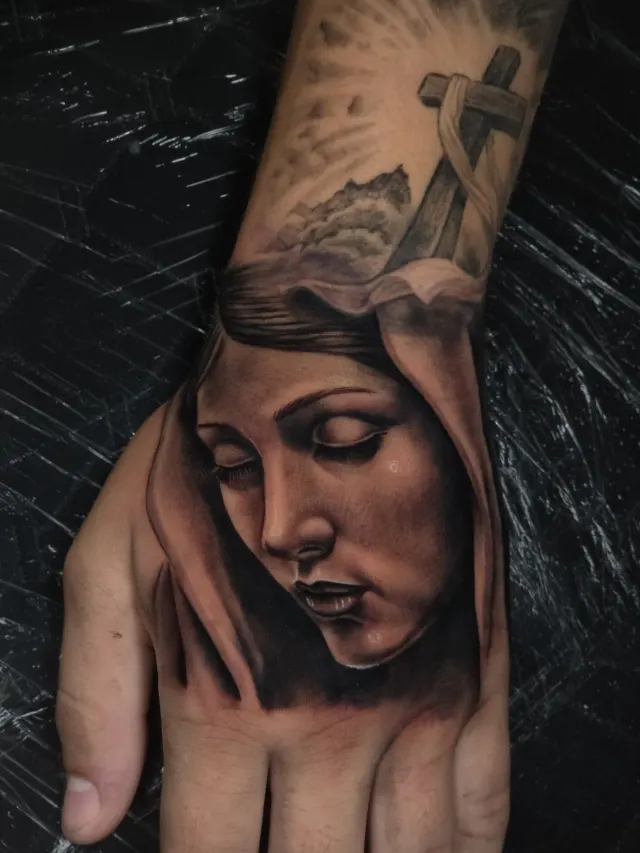 Tatuagem de rosto feminino com cruz em realismo se estendendo até a mão